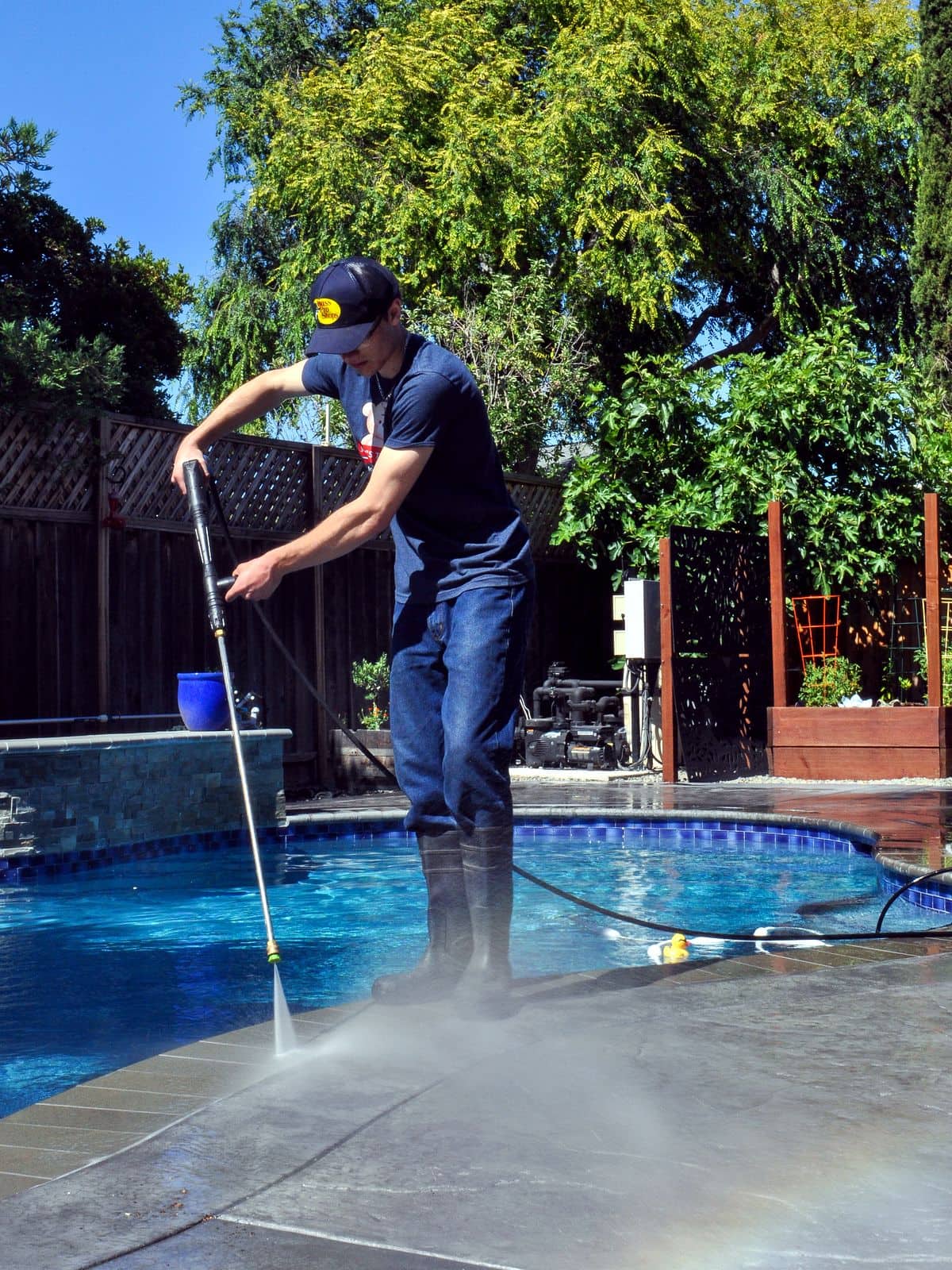 Bay Area Exterior Cleaning's owner pressure washing a backyard pool deck, with cleaning mist rising from the concrete.